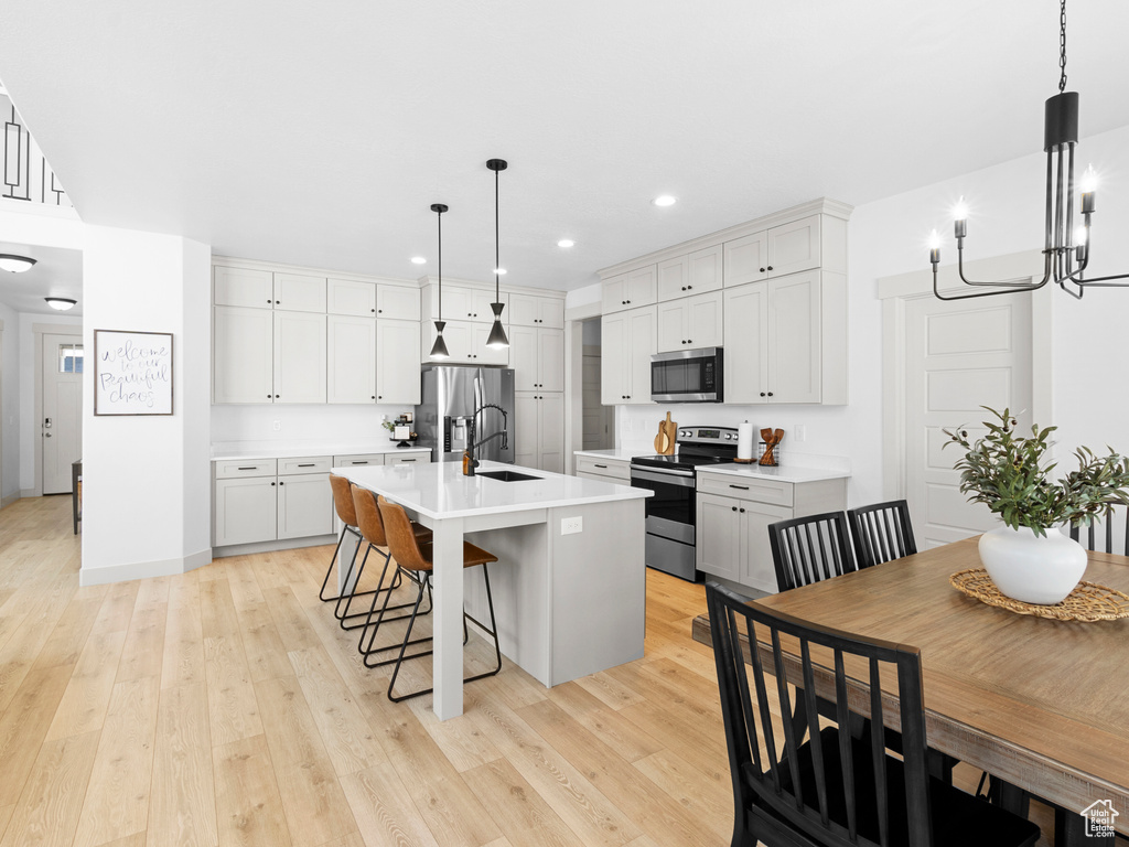 Kitchen with decorative light fixtures, a breakfast bar, appliances with stainless steel finishes, an island with sink, and light wood-type flooring