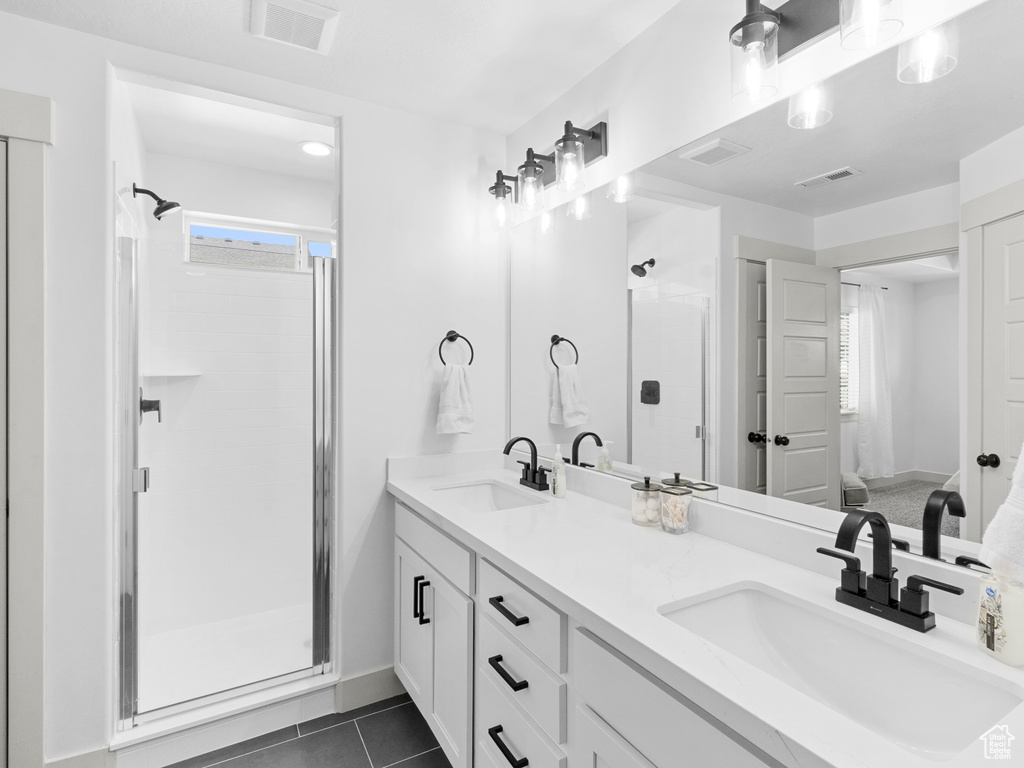 Bathroom with tile flooring, a shower with door, and double sink vanity