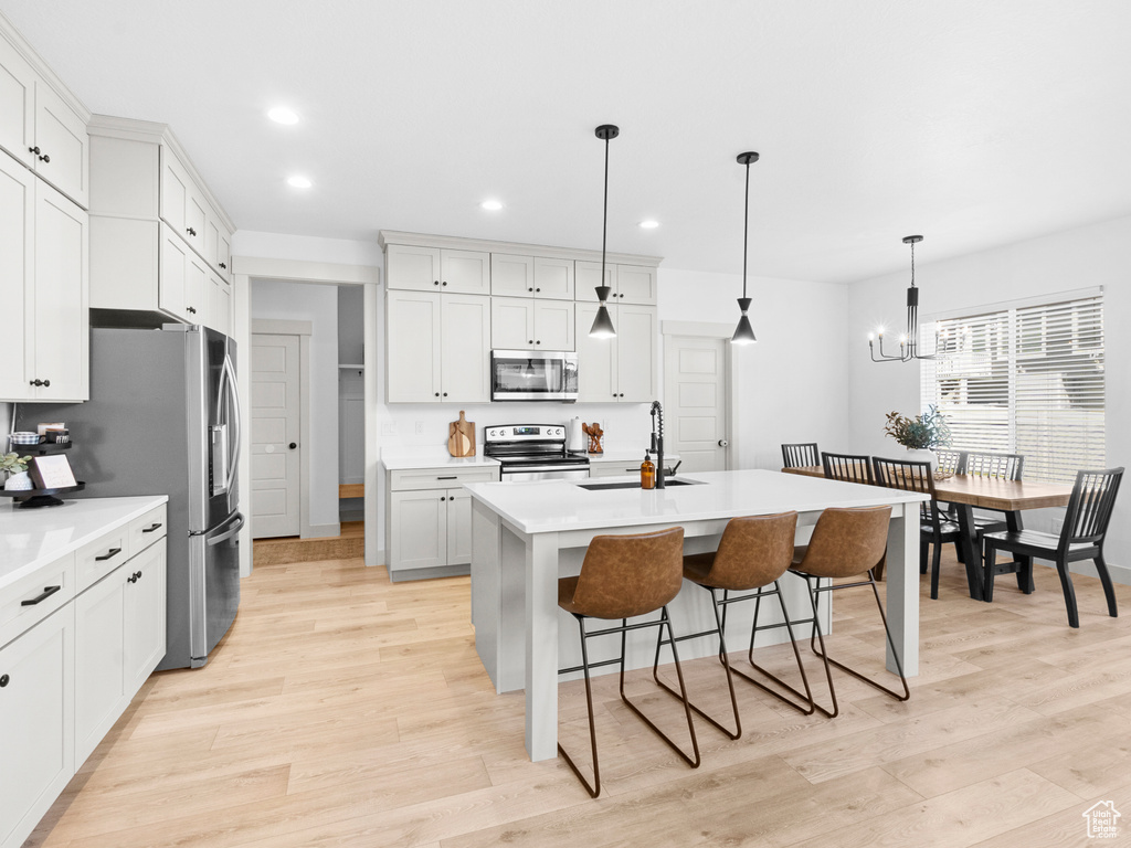 Kitchen featuring appliances with stainless steel finishes, a kitchen bar, pendant lighting, light hardwood / wood-style flooring, and a kitchen island with sink