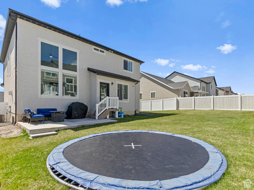 Back of property with outdoor lounge area, a patio, a yard, and a trampoline