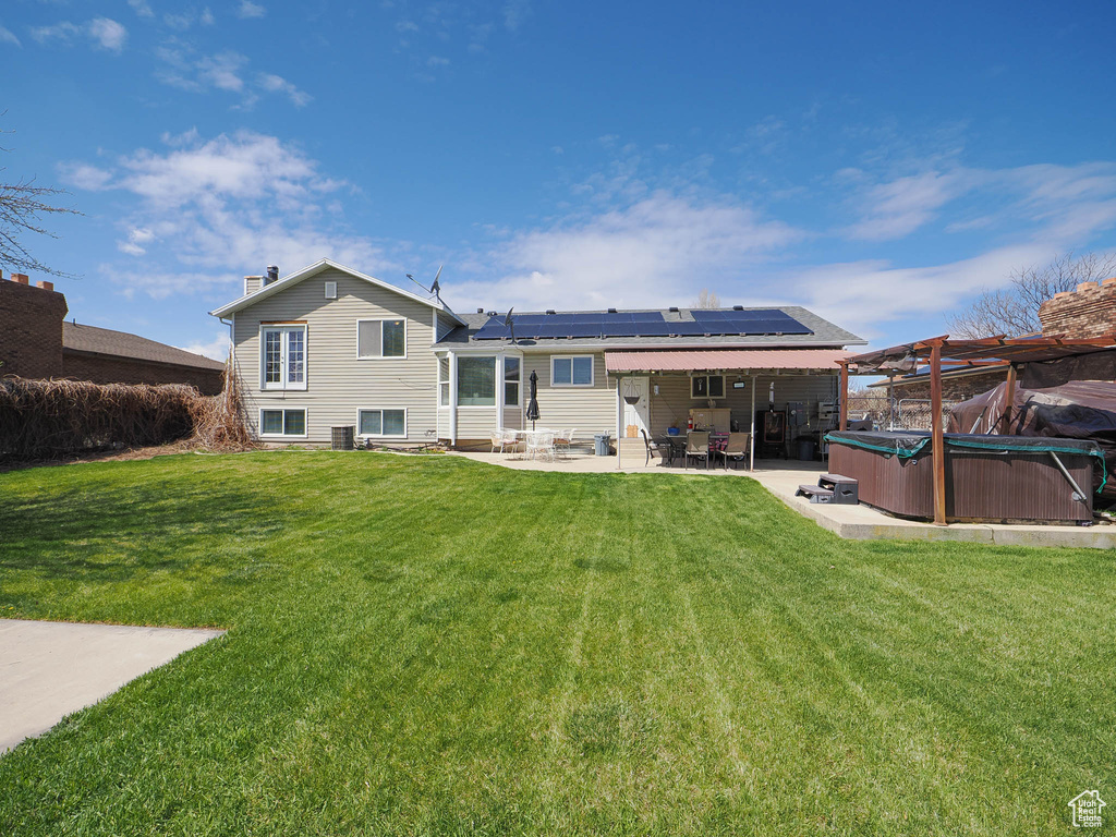 Rear view of property with solar panels, a lawn, a patio area, and a hot tub
