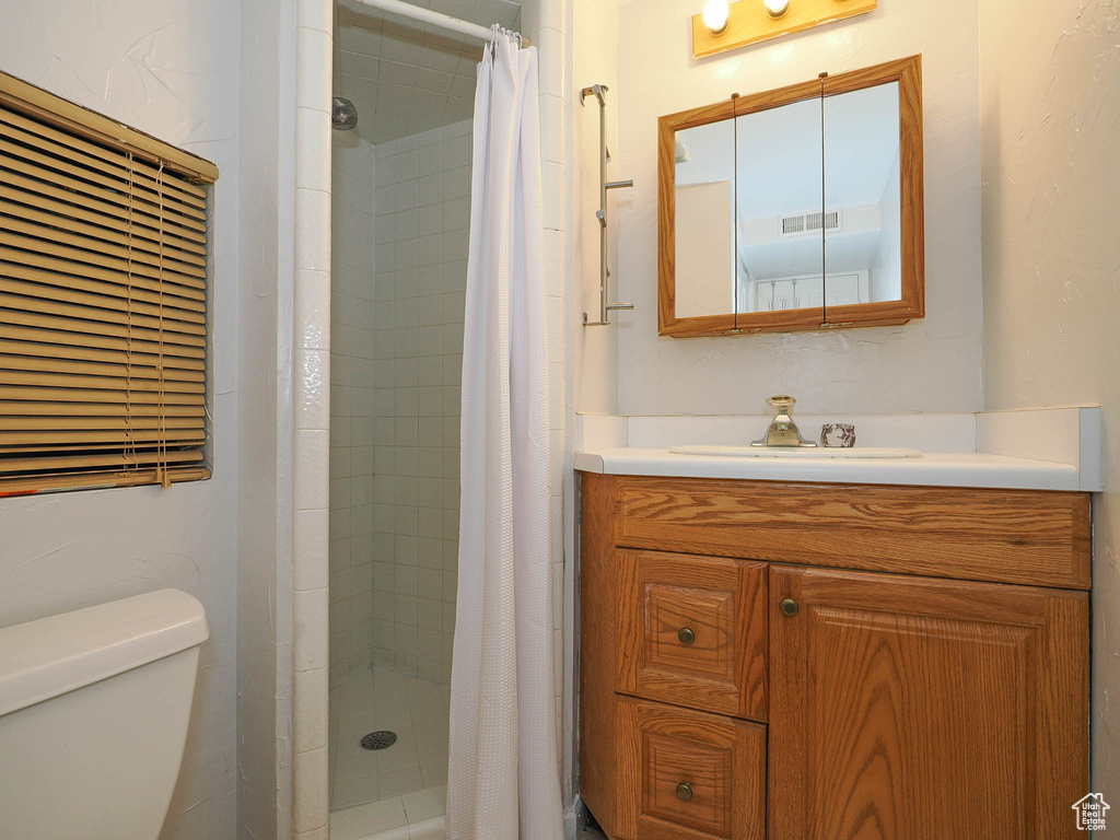 Bathroom featuring curtained shower, toilet, and vanity