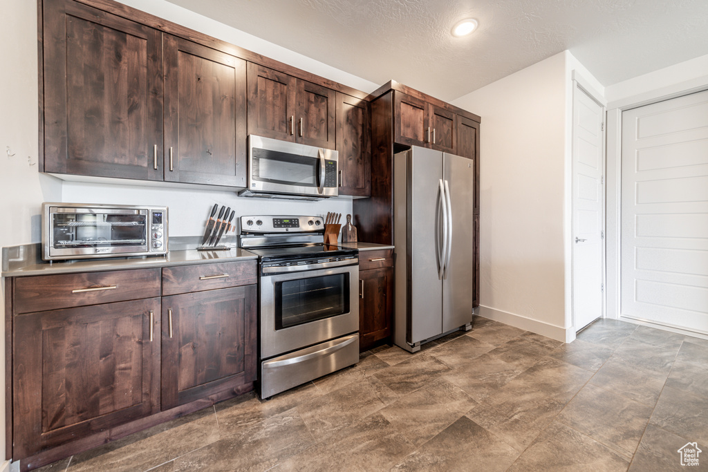 Kitchen featuring stainless steel appliances, dark tile flooring, and dark brown cabinetry