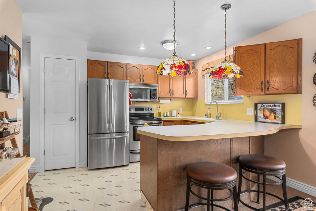 Kitchen featuring decorative light fixtures, appliances with stainless steel finishes, a breakfast bar area, light tile floors, and kitchen peninsula