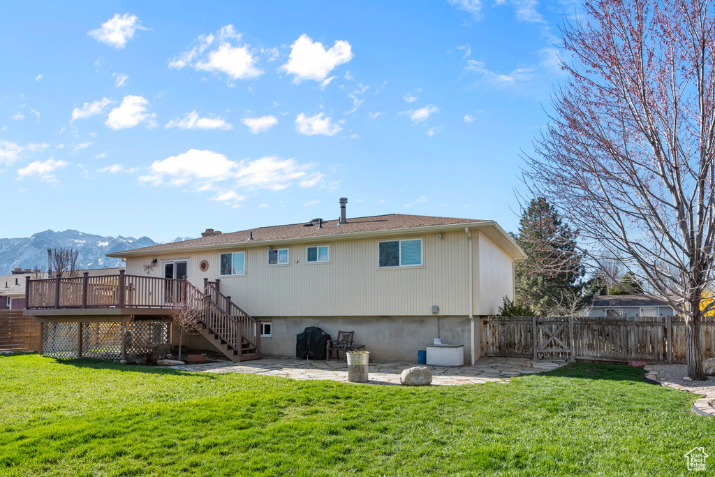 Rear view of property with a deck with mountain view, a lawn, and a patio