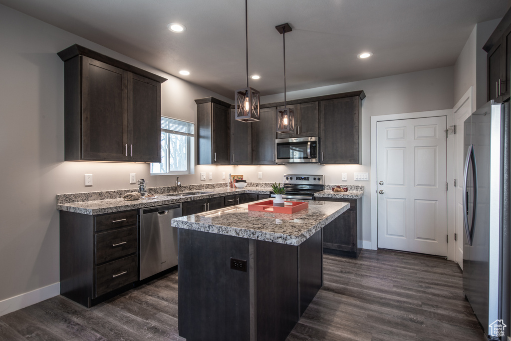 Kitchen with dark hardwood / wood-style flooring, decorative light fixtures, appliances with stainless steel finishes, dark brown cabinetry, and a kitchen island