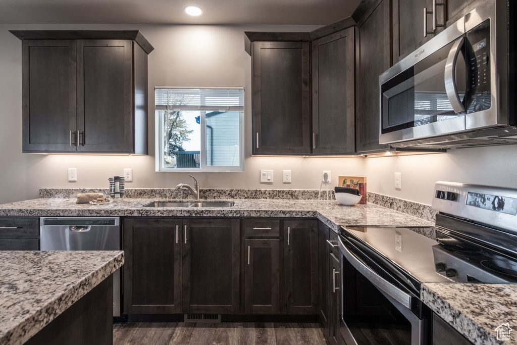 Kitchen featuring dark hardwood / wood-style flooring, appliances with stainless steel finishes, light stone counters, and sink