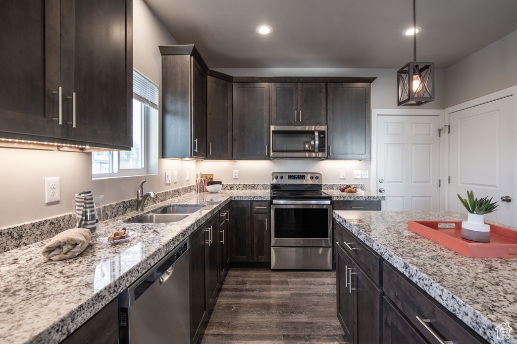 Kitchen with appliances with stainless steel finishes, pendant lighting, dark brown cabinets, and light stone countertops