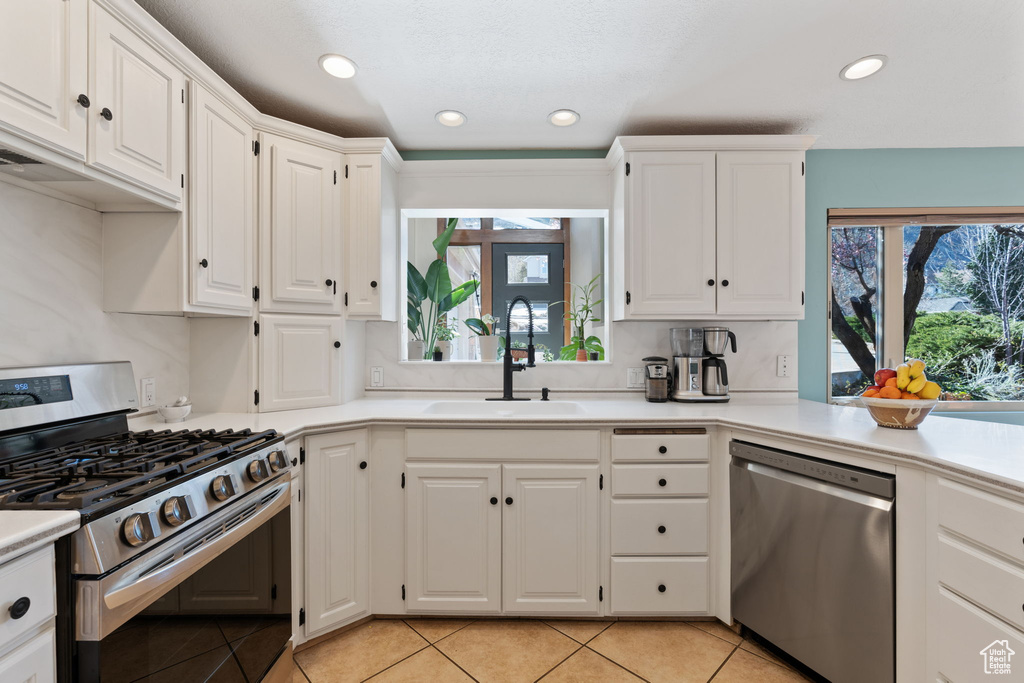 Kitchen featuring white cabinets, light tile floors, stainless steel appliances, and plenty of natural light
