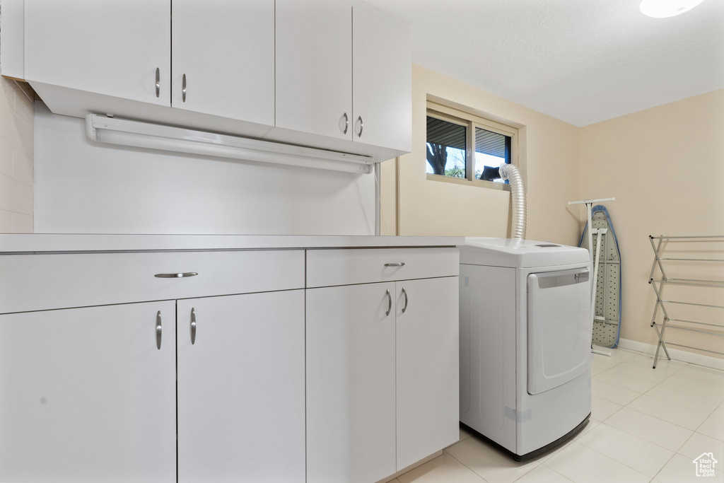Clothes washing area with cabinets, washer / clothes dryer, and light tile floors