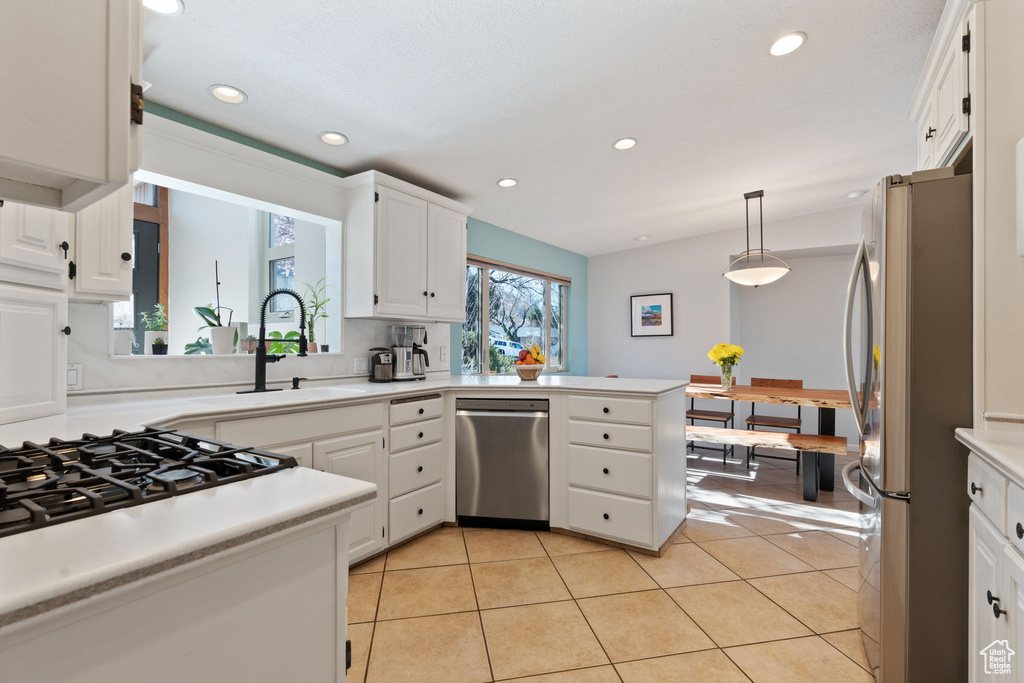Kitchen featuring white cabinets, kitchen peninsula, appliances with stainless steel finishes, light tile flooring, and hanging light fixtures