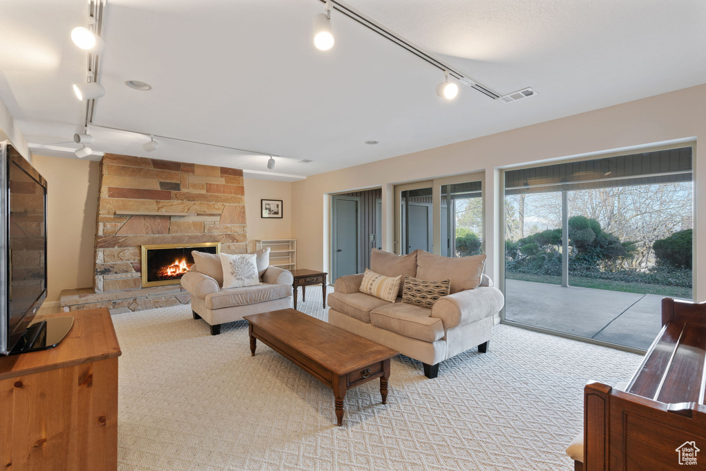 Living room featuring ceiling fan, a stone fireplace, light carpet, and rail lighting
