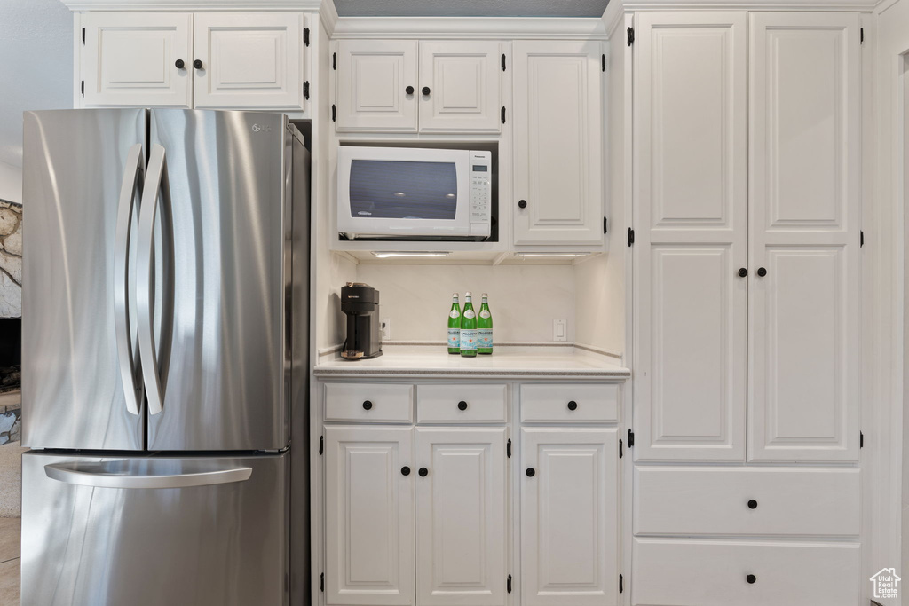 Kitchen with white microwave, stainless steel refrigerator, and white cabinetry