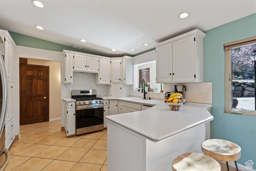 Kitchen with sink, a wealth of natural light, kitchen peninsula, and stainless steel gas range oven