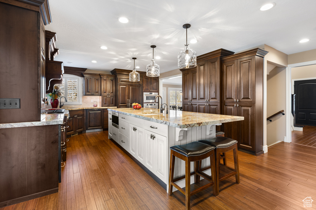 Kitchen featuring a center island with sink, decorative light fixtures, dark brown cabinets, white cabinetry, and dark hardwood / wood-style floors