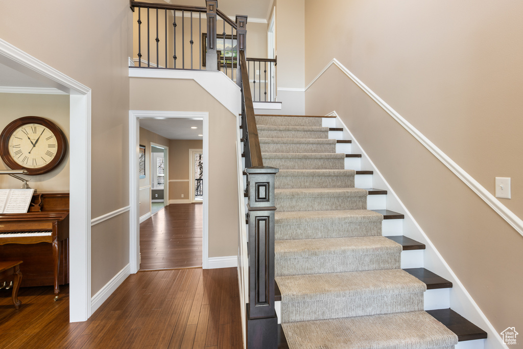 Stairs featuring dark wood-type flooring, ornamental molding, and a towering ceiling