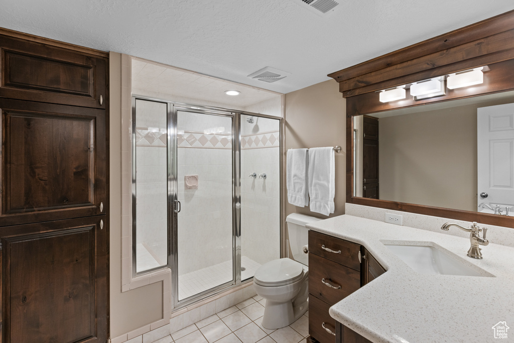 Bathroom with toilet, vanity, a shower with shower door, and tile floors