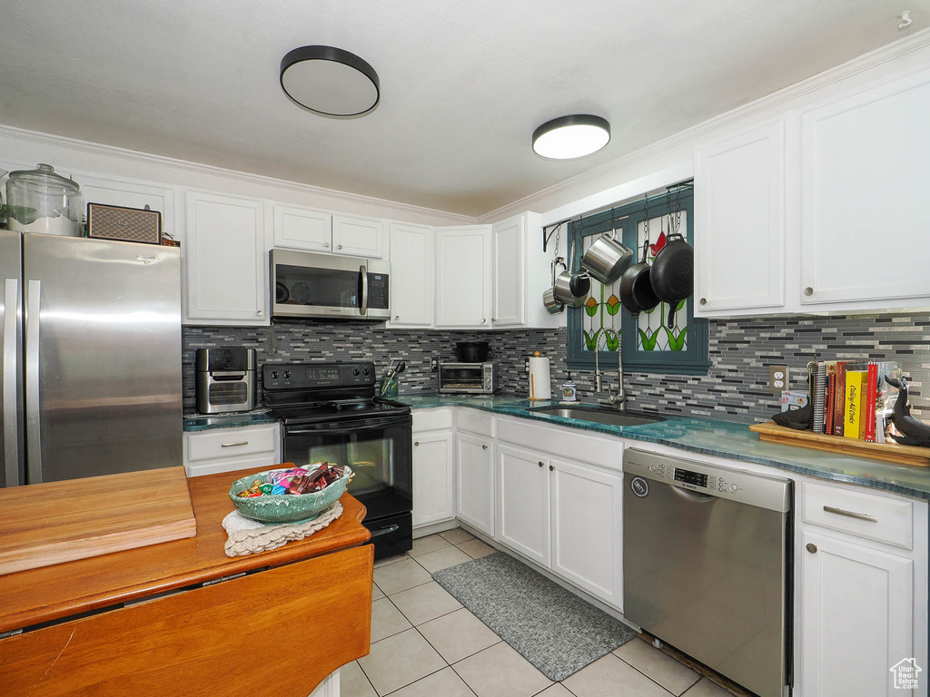 Kitchen featuring appliances with stainless steel finishes, tasteful backsplash, white cabinets, light tile floors, and sink