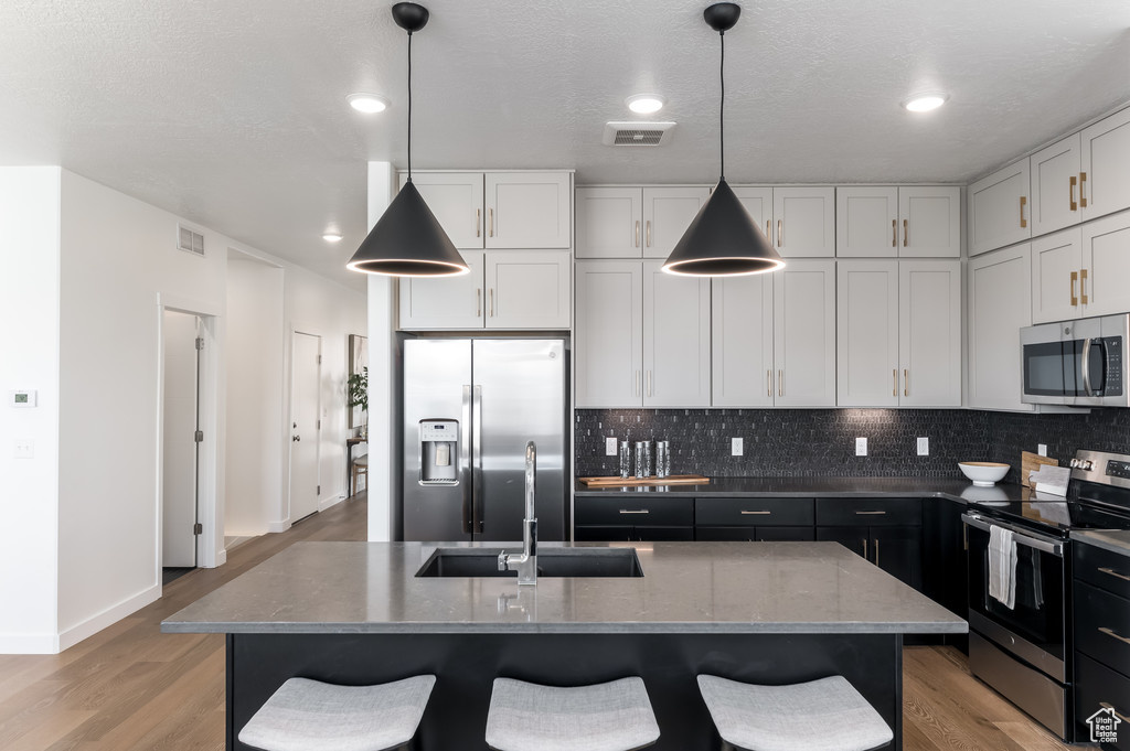 Kitchen with appliances with stainless steel finishes, backsplash, light hardwood / wood-style floors, and hanging light fixtures