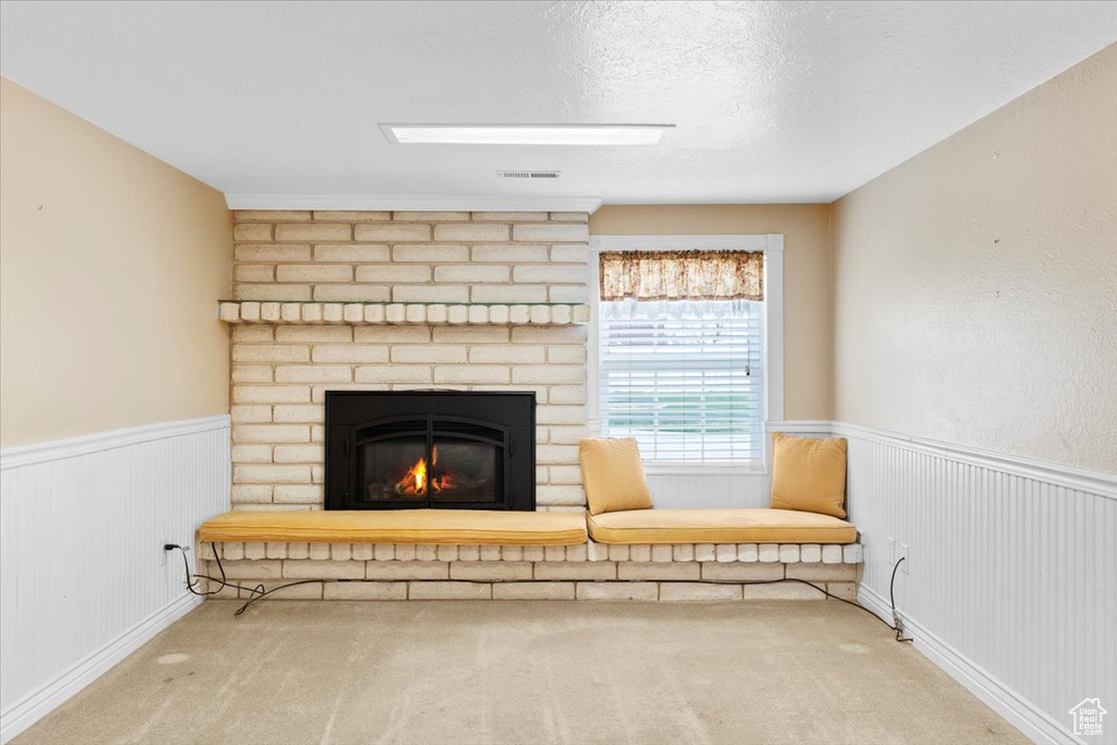 Unfurnished living room with light colored carpet, a textured ceiling, brick wall, and a brick fireplace