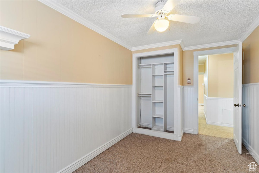 Unfurnished bedroom with ceiling fan, a closet, a textured ceiling, light colored carpet, and ornamental molding