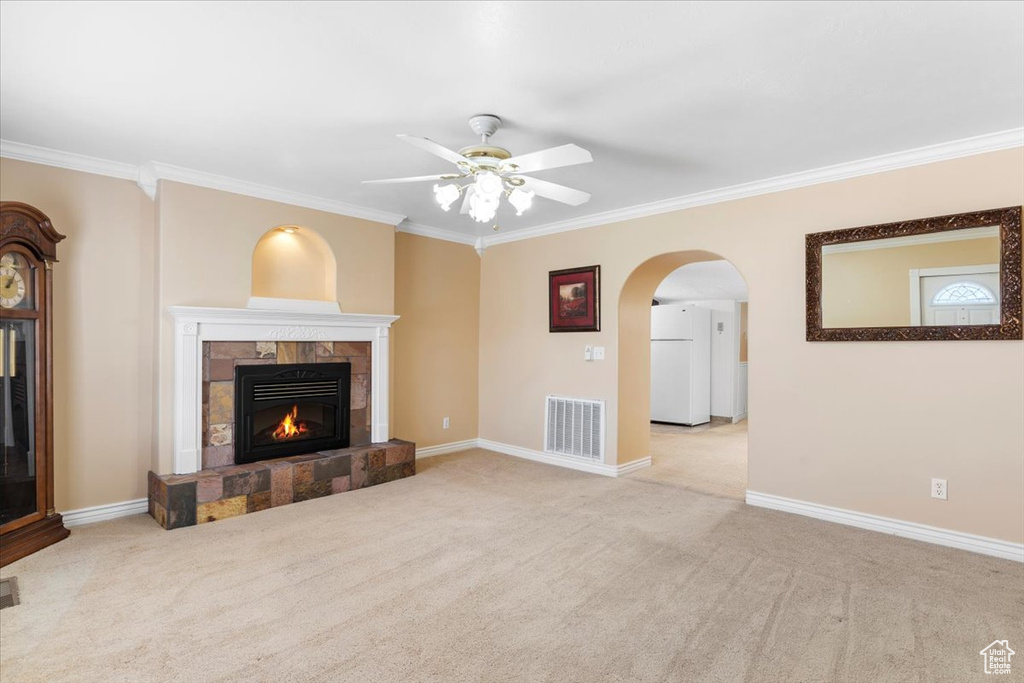 Unfurnished living room featuring ceiling fan, a tile fireplace, ornamental molding, and light carpet