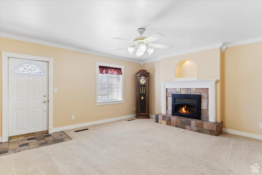Unfurnished living room with a tiled fireplace, ceiling fan, ornamental molding, and light carpet