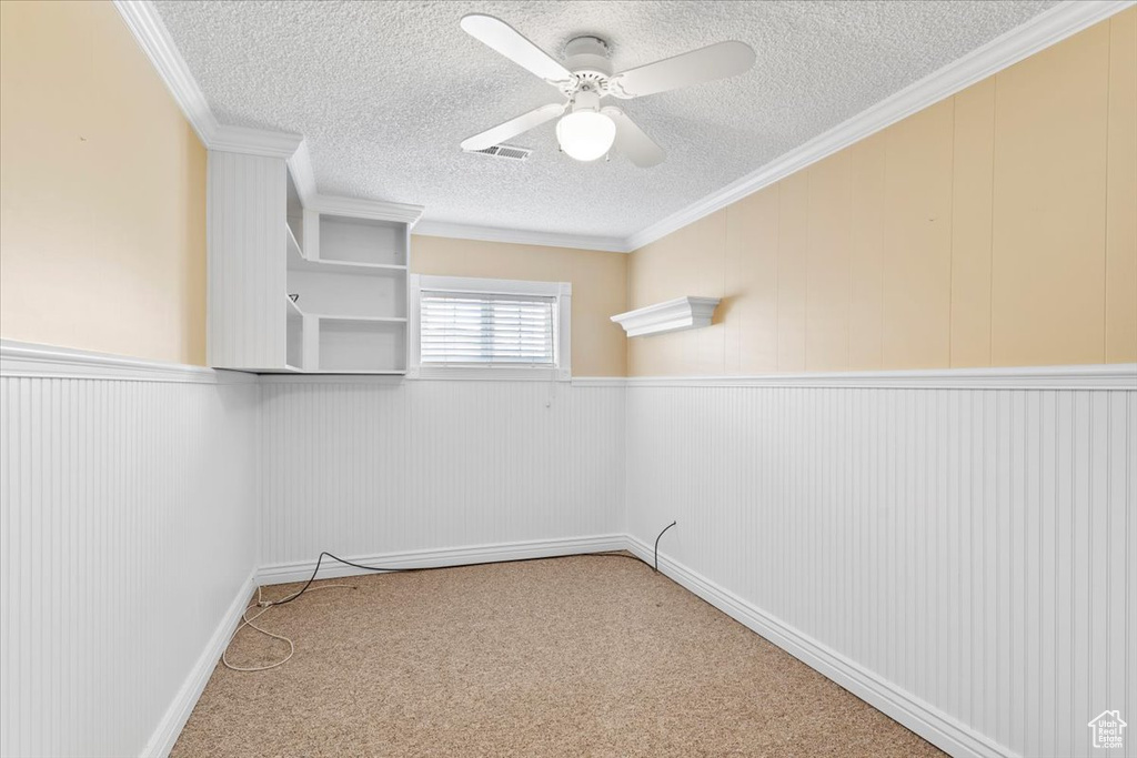 Carpeted empty room featuring ceiling fan, a textured ceiling, and crown molding