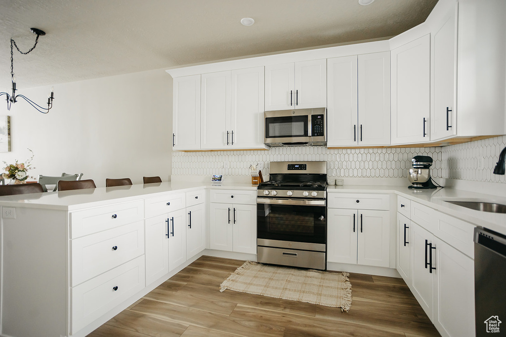Kitchen with light hardwood / wood-style floors, tasteful backsplash, stainless steel appliances, and white cabinetry