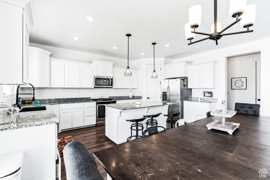 Kitchen with pendant lighting, dark wood-type flooring, appliances with stainless steel finishes, a breakfast bar area, and a kitchen island