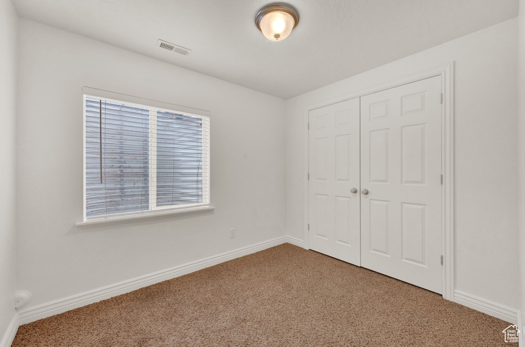 Unfurnished bedroom with a closet, dark carpet, and multiple windows
