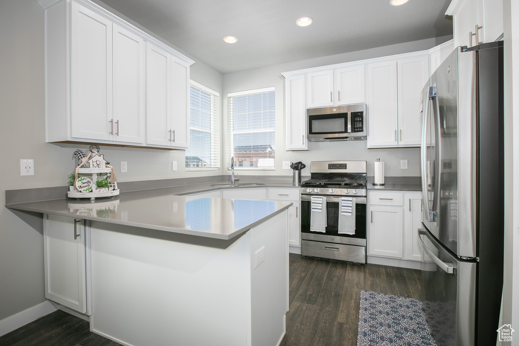 Kitchen featuring white cabinets, kitchen peninsula, appliances with stainless steel finishes, sink, and dark hardwood / wood-style floors