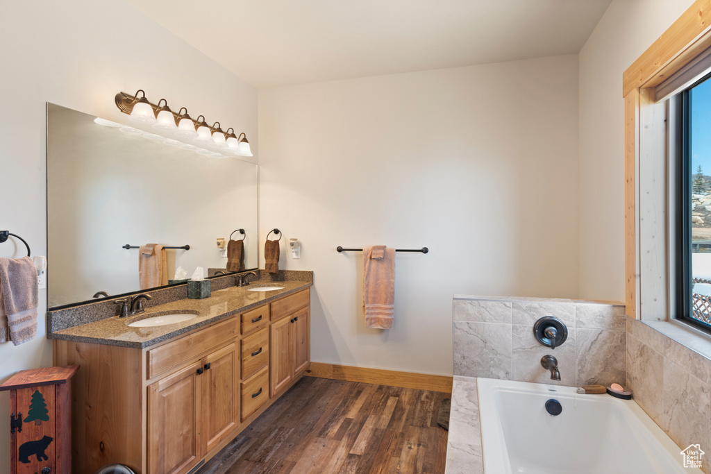 Bathroom featuring hardwood / wood-style floors, double sink, vanity with extensive cabinet space, and a washtub