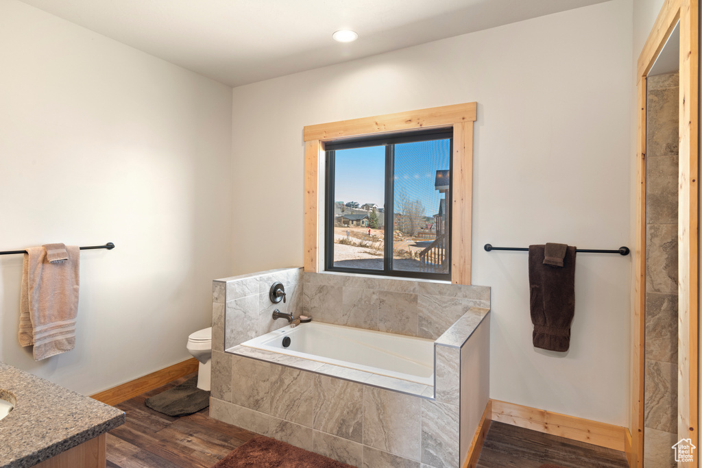Bathroom featuring toilet, wood-type flooring, vanity, and tiled tub