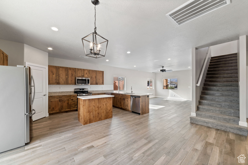 Kitchen with decorative light fixtures, light hardwood / wood-style floors, stainless steel appliances, a center island, and ceiling fan with notable chandelier