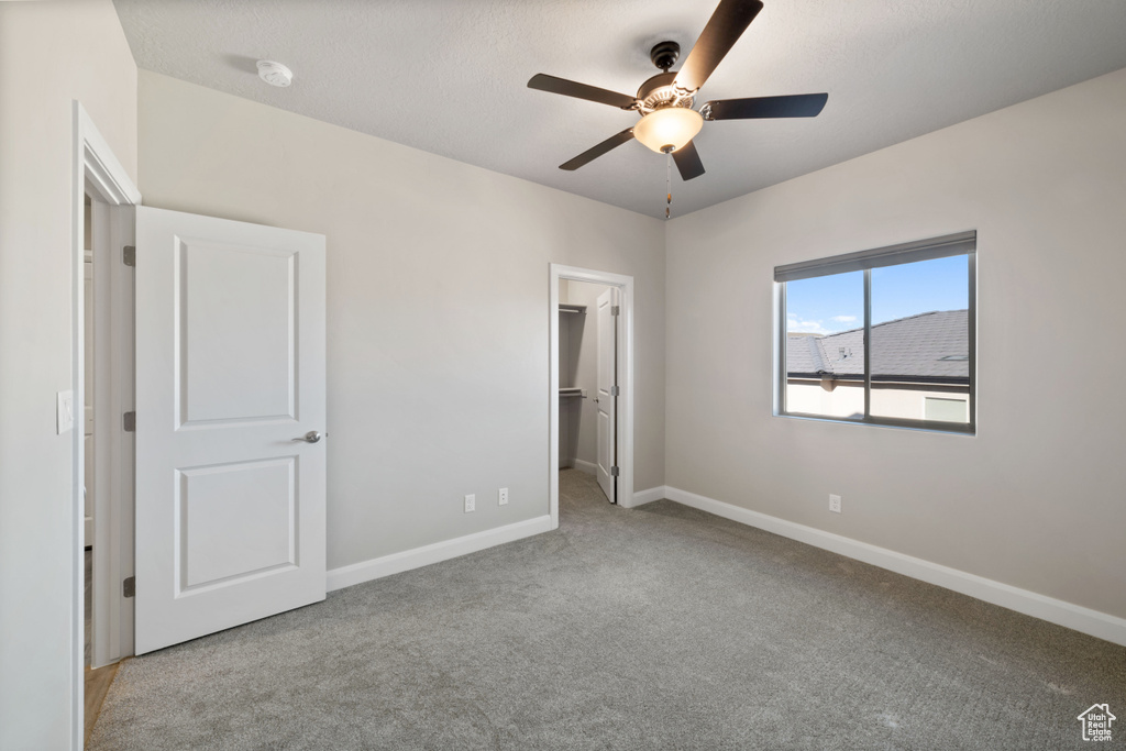 Unfurnished bedroom featuring ceiling fan, a spacious closet, light carpet, and a closet