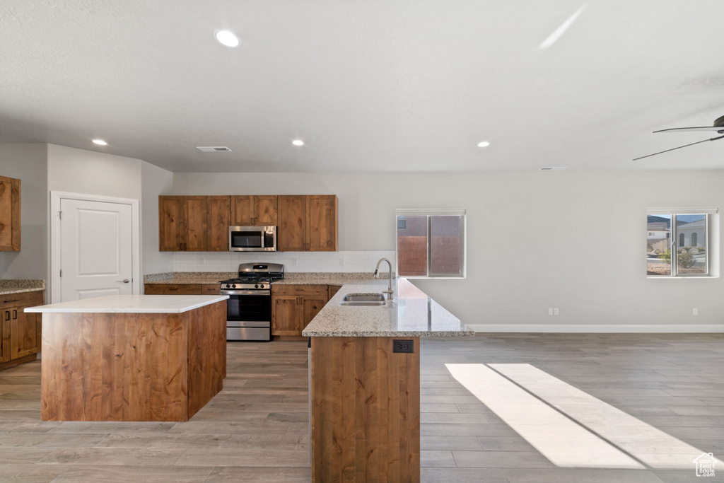 Kitchen featuring appliances with stainless steel finishes, light hardwood / wood-style floors, and a center island with sink
