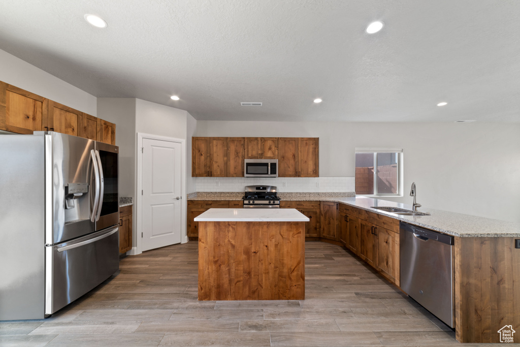 Kitchen featuring appliances with stainless steel finishes, sink, light hardwood / wood-style flooring, and a center island