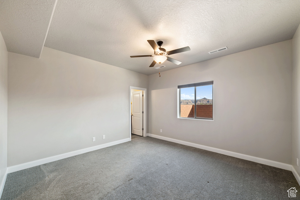 Empty room with a textured ceiling, carpet floors, and ceiling fan