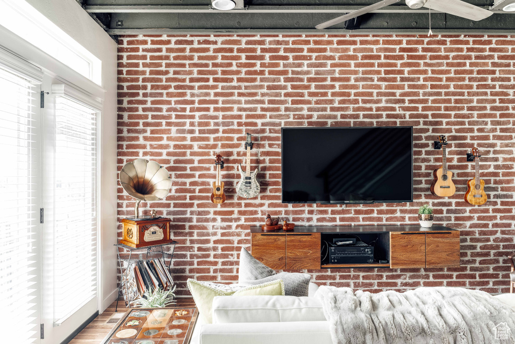Living room with brick wall, hardwood / wood-style floors, and ceiling fan
