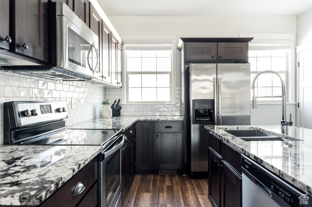 Kitchen featuring appliances with stainless steel finishes, light stone counters, a wealth of natural light, and dark hardwood / wood-style flooring