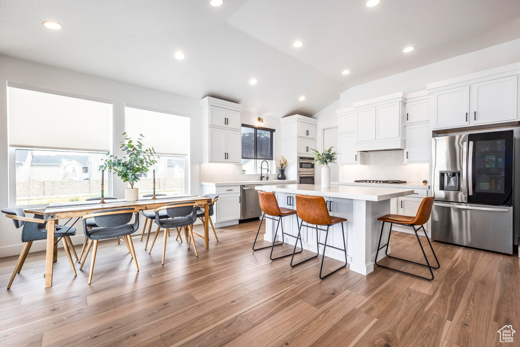 Kitchen featuring a kitchen island, light hardwood / wood-style floors, stainless steel appliances, and a kitchen breakfast bar