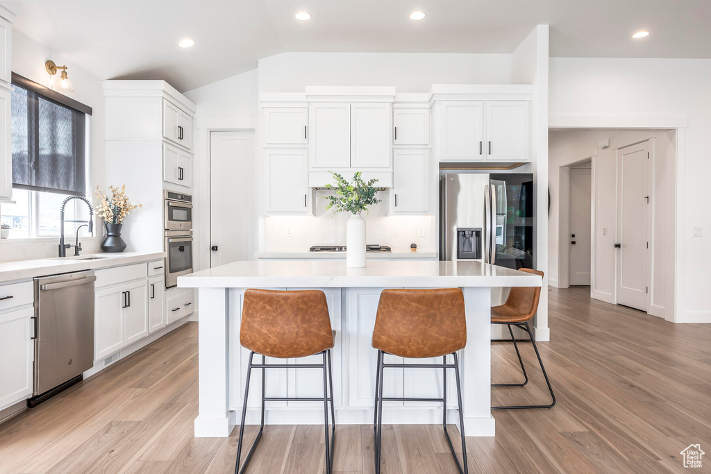 Kitchen featuring a kitchen island, stainless steel appliances, light hardwood / wood-style floors, and white cabinetry