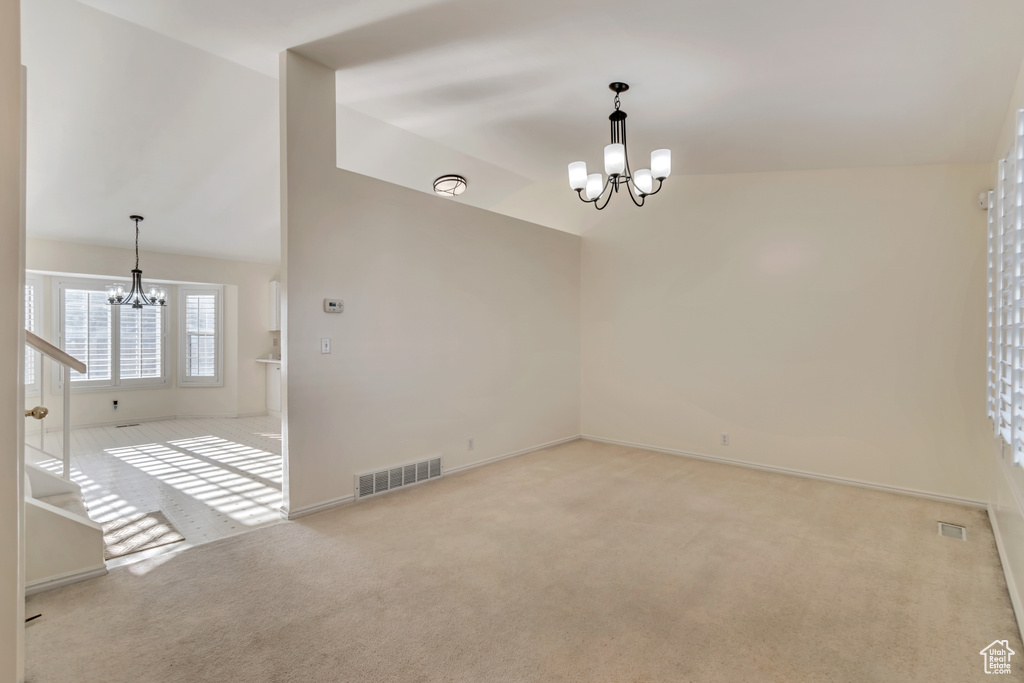 Carpeted empty room with vaulted ceiling and a chandelier