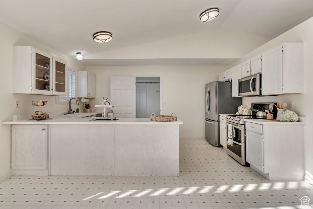 Kitchen featuring appliances with stainless steel finishes, lofted ceiling, white cabinetry, and kitchen peninsula
