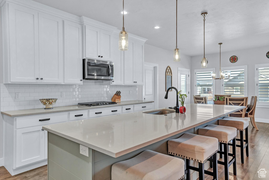 Kitchen with a kitchen bar, stainless steel appliances, sink, a kitchen island with sink, and hanging light fixtures