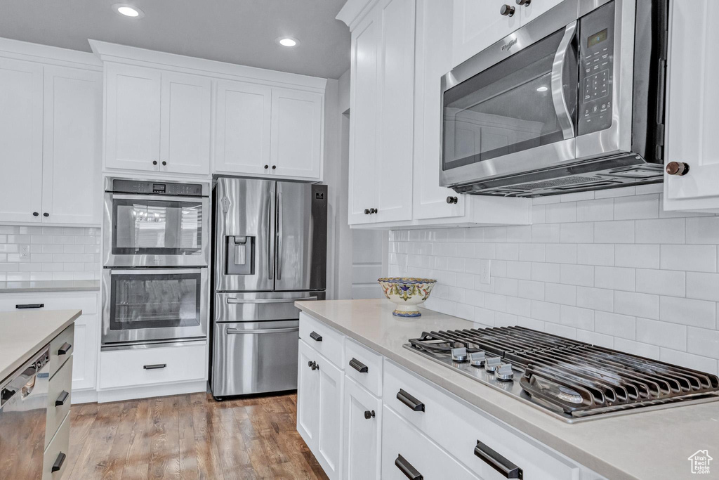 Kitchen featuring stainless steel appliances, light wood-type flooring, white cabinets, and backsplash