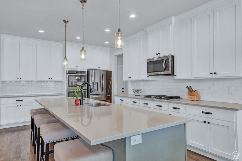 Kitchen with backsplash, appliances with stainless steel finishes, and an island with sink