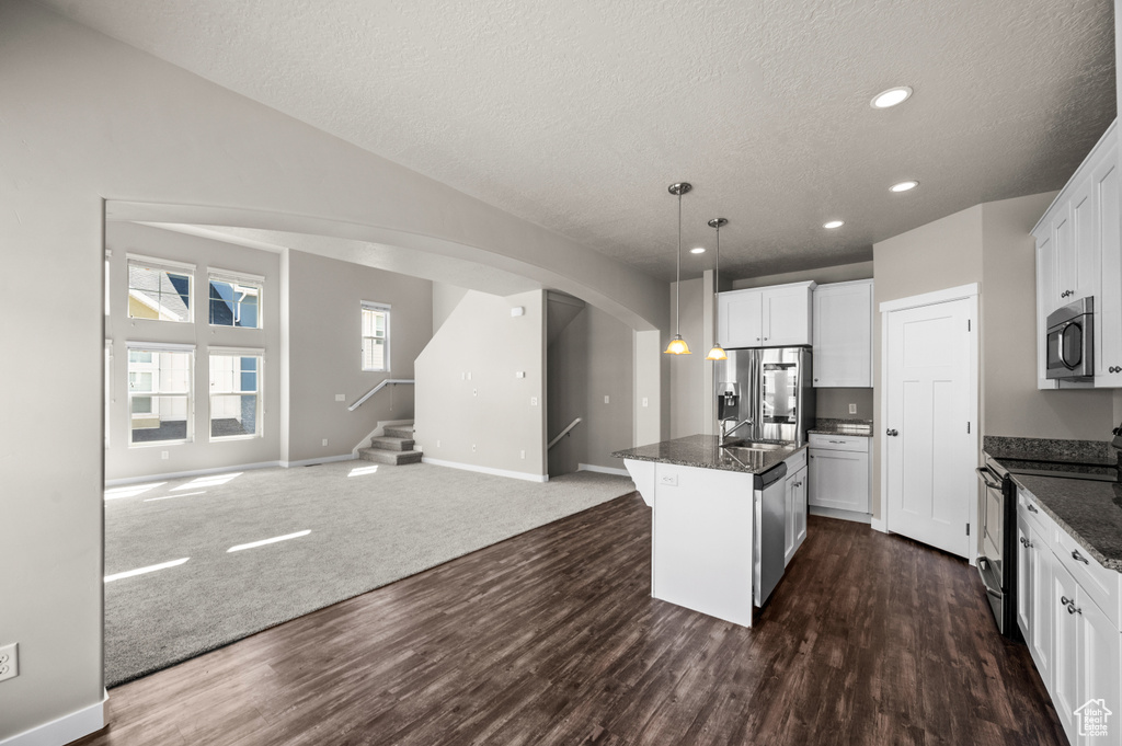 Kitchen featuring appliances with stainless steel finishes, white cabinetry, a center island with sink, dark colored carpet, and pendant lighting