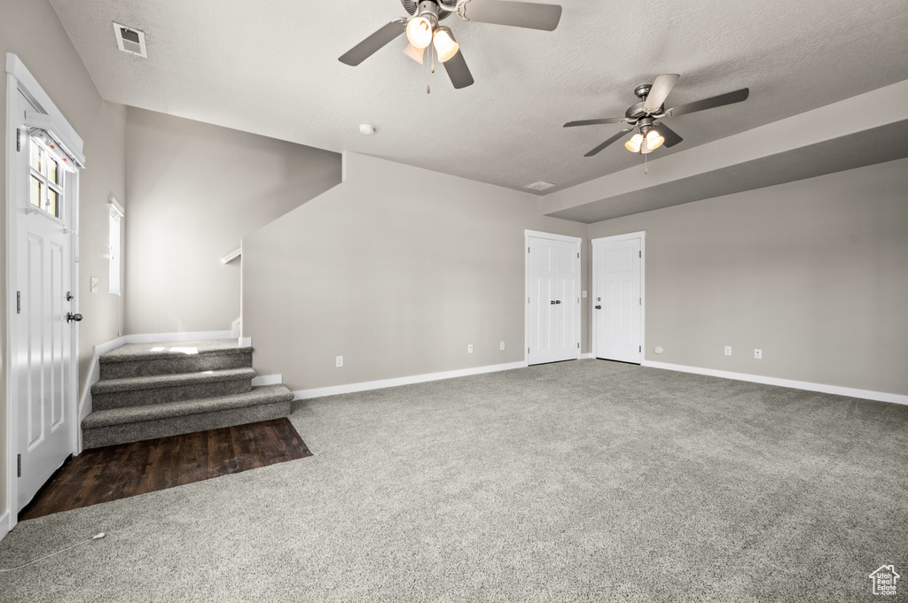 Unfurnished living room with ceiling fan and dark colored carpet